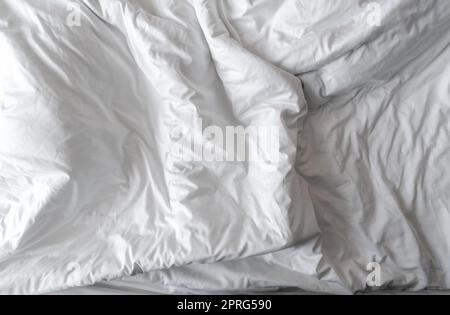 Couverture en lin blanc dans la chambre d'hôtel. Détail gros plan de couverture blanche désordonnée. Lit confortable avec couette blanche douce. Dormez à poings fermés avec une literie de bonne qualité. Couverture blanche plissée. Banque D'Images