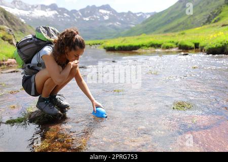 Randonneur remplissant la cantine d'eau brute dans une rivière Banque D'Images