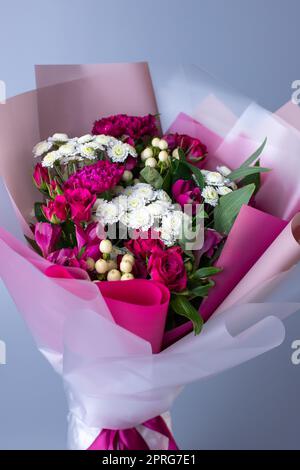 Bouquet de fleurs roses et blanches enveloppées de papier floral sur fond bleu. Banque D'Images