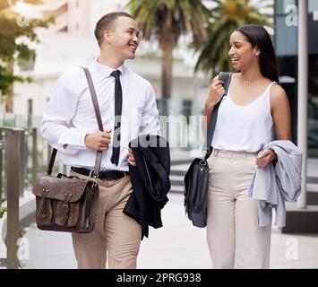 Affaires, femme et homme avec un sourire marchant pour travailler au bureau ou à la compagnie dans la rue de la ville. Des personnes, des communications ou des collègues heureux, des collègues ou des travailleurs ou des employés qui se rendent dans le bâtiment de l'entreprise. Banque D'Images