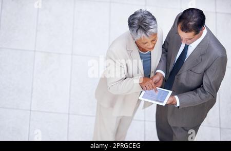 Des idées qui se rebondissent les unes sur les autres. Prise de vue en grand angle de deux collègues professionnels se tenant debout avec une tablette numérique et discutant du travail. Banque D'Images