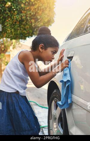 S'assurer qu'elle ne manque pas une place. Une jeune fille s'occupe de nettoyer une voiture à l'extérieur. Banque D'Images