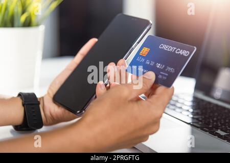 Une femme tient sa carte de crédit et son smartphone pour acheter un produit à la maison Banque D'Images