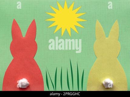 Un lapin en papier rouge et un lapin jaune sur fond vert avec soleil et herbe illustrés Banque D'Images