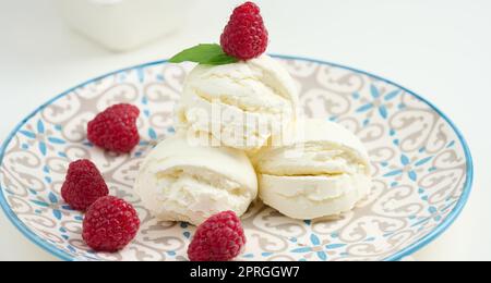 Boules de glace à la vanille aux framboises rouges dans une assiette ronde Banque D'Images