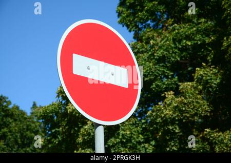 Une circulaire panneau rouge avec une barre blanche indiquant pas d'entrée sur un métal gris contre un des arbres vert et bleu ciel clair Banque D'Images