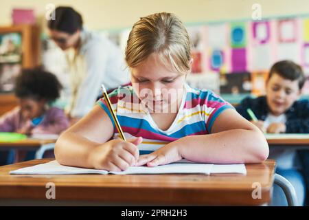 Cette question est un peu difficile. une jeune fille assise dans sa salle de classe à l'école et écrivant dans son cahier d'exercices Banque D'Images