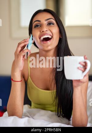 La motivation matinale d'un bon appel de nouvelles. Une jeune femme heureuse parlant au téléphone au lit. Banque D'Images