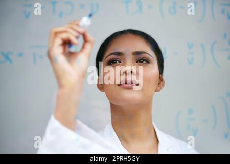 Une jeune scientifique attirante travaillant sur un mur de verre dans son laboratoire travaille sur la formule pour un remède. Banque D'Images