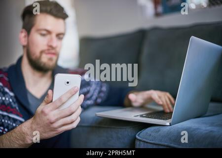 Connecter ses appareils au wifi. Un beau jeune homme utilisant un ordinateur portable et un téléphone portable à la maison. Banque D'Images