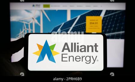 Personne tenant un téléphone portable avec le logo de la société américaine alliant Energy Corporation à l'écran en face de la page Web d'affaires. Mise au point sur l'affichage du téléphone. Banque D'Images