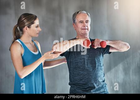 S'engage à garder actif et fort à tout âge. Un homme âgé utilisant des poids avec l'aide d'un thérapeute physique. Banque D'Images