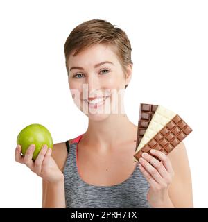 Vous avez toujours le choix. Portrait studio d'une jeune femme en forme de femme décidant de manger du chocolat ou une pomme sur un fond blanc. Banque D'Images