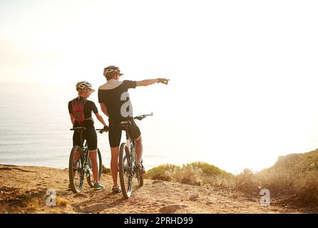 Le vélo est la liberté. Un jeune couple admirant la vue depuis une colline pendant une balade en vélo. Banque D'Images