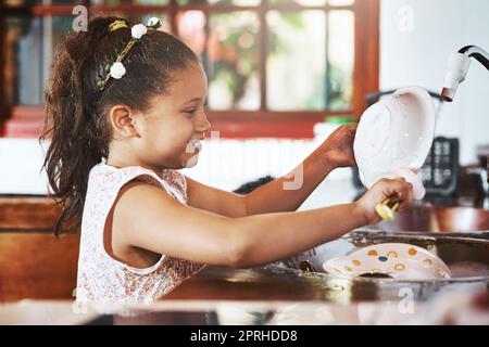 Elle a toujours été un enfant serviable. Une adorable petite fille lavant des plats à la maison. Banque D'Images