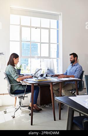 S'engage à faire de leur mieux. Collègues travaillant sur leurs ordinateurs à un bureau dans un bureau ouvert. Banque D'Images