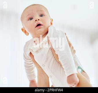 Le monde semble assez intéressant d'ici. Un adorable bébé garçon étant tenu par sa mère à la maison. Banque D'Images