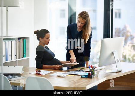 Trouver un équilibre entre le travail et l'attente. Une femme d'affaires enceinte et un collègue utilisent une tablette numérique ensemble dans un bureau. Banque D'Images