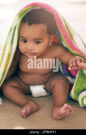 Quelqu'un m'a fait sortir ici. Une adorable petite fille couverte d'une couverture colorée à la maison. Banque D'Images