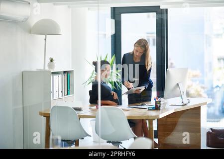 Signature du dernier projet. Une femme d'affaires enceinte et un collègue utilisant une tablette numérique ensemble dans un bureau. Banque D'Images