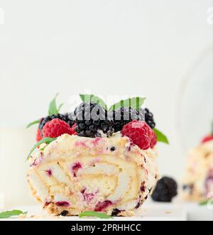 Rouleau de meringue cuit avec crème et fruits frais sur un plateau en bois blanc, délicieux dessert Banque D'Images