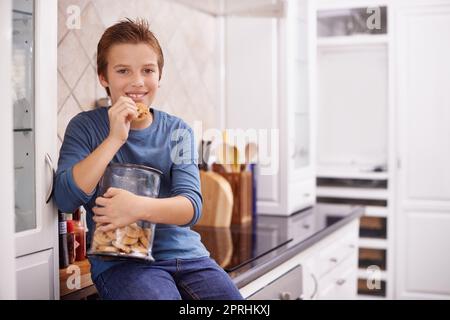 Un autre ne fera pas de mal. Un jeune garçon mangeant un cookie tout en tenant un pot à biscuits Banque D'Images