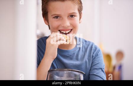 Yum yum. Un jeune garçon mangeant un cookie tout en tenant un pot à biscuits Banque D'Images