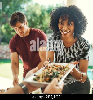 Une bonne cuisine réunit toujours tout le monde. une belle jeune femme qui passe devant une assiette de nourriture à une famille qui se réunit à l'extérieur Banque D'Images