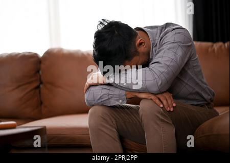 Un homme asiatique millénaire stressé et déprimé pleure sur le canapé dans un salon, souffrant de sa vie infructueuse ou de son échec professionnel. Banque D'Images