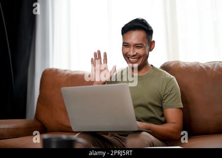 Homme asiatique professionnel et intelligent du millénaire ayant une réunion en ligne avec son équipe tout en travaillant de chez lui. concept de travail à distance Banque D'Images