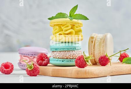 Une pile de macarons multicolores et de framboises rouges sur fond blanc. Banque D'Images