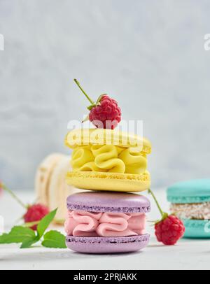 Une pile de macarons multicolores et de framboises rouges sur fond blanc. Banque D'Images