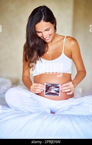 Première image de Babys une femme enceinte tenant une image d'échographie devant son ventre. Banque D'Images
