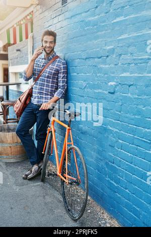 Je me suis happé sur mon vélo maintenant. Un beau jeune homme se penchait contre un mur avec son vélo parlant sur un téléphone portable. Banque D'Images