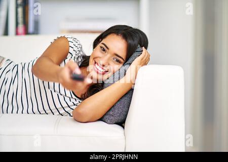 Changement de chaîne. Portrait court d'une jeune femme regardant la télévision tout en se relaxant sur son canapé à la maison. Banque D'Images