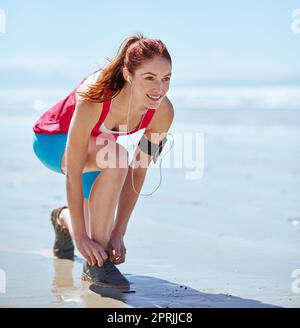 Préparation pour un entraînement. Prise de vue en longueur d'une jeune femme qui noue ses lacets tout en courant sur la plage. Banque D'Images