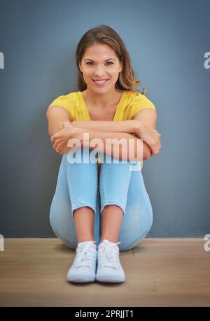 Ne vous arrêtez jamais de sourire. Une jeune femme assise contre un mur gris. Banque D'Images
