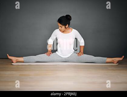 Une jeune femme attirante qui fait les fractionnements de sa routine de yoga fait une bonne séance de musculation. Banque D'Images