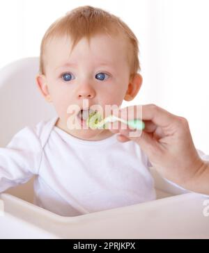 Essayons. Un bébé mignon recevant une cuillerée de nourriture de sa mère Banque D'Images