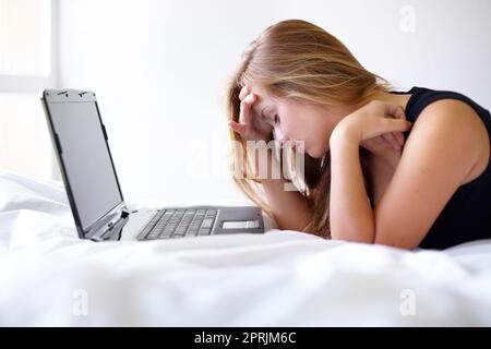 Ma tête a l'impression d'exploser. une belle jeune femme qui a l'air frustrée d'utiliser un ordinateur portable sur son lit Banque D'Images