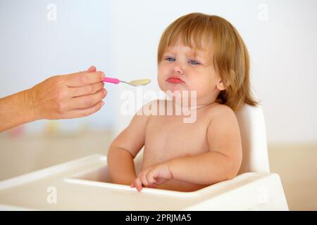 Frustrations liées au temps d'alimentation. Mignonne bébé fille semble misérable tandis que sa main de mère lui offre un peu de nourriture sur une cuillère Banque D'Images