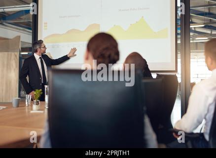Il a toute l'attention dans la réunion. Un cadre donne une présentation sur un écran de projection à un groupe de collègues dans une salle de réunion. Banque D'Images