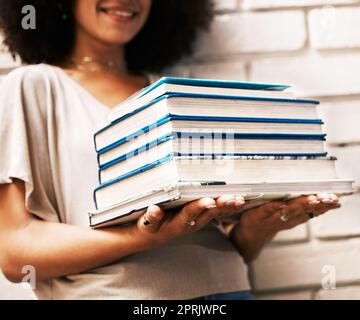 Éducation, connaissances et apprentissage étudiant avec des livres pour étudier, la recherche ou l'affectation sur un mur blanc. Bourse noire, fille géek ou nerd avec pile de manuels de bibliothèque universitaire pour la lecture Banque D'Images