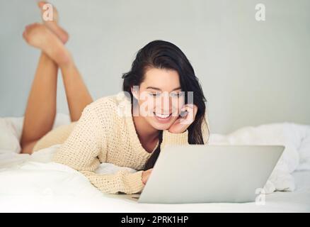 Elle a suivi tous ses réseaux sociaux. Une jeune femme qui utilise son ordinateur portable tout en étant allongé sur son lit. Banque D'Images