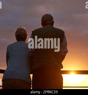 Des moments inoubliables. Vue arrière d'un couple âgé regardant le coucher du soleil ensemble Banque D'Images