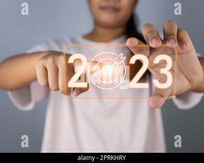 Une femme qui pointe vers l'icône du dart Board représente l'établissement des objectifs pour 2023, le concept de démarrage, la planification financière, la stratégie de développement, l'objectif d'affaires se Banque D'Images