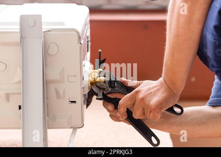 L'homme tient la clé dans sa main. Un technicien mâle utilise une clé pour installer un système de climatisation moderne. Un employé de la rue installe un cond. D'air extérieur Banque D'Images