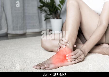 Douleur au pied, la femme maintient sa blessure à la cheville sensation de douleur dans son pied à la maison, la femme souffrant de douleur aux pieds utilisation massage des mains détendre le muscle de la cheville dans Banque D'Images