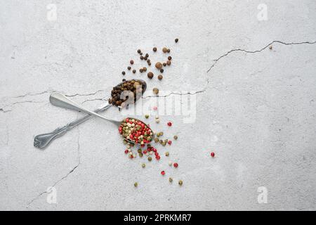 Deux cuillères croisées avec différentes sortes de poivre sur béton arrière-plan Banque D'Images