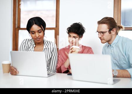 La communication est essentielle à la réussite. un groupe diversifié d'hommes d'affaires assis ensemble et utilisant leur ordinateur portable lors d'une réunion au bureau Banque D'Images